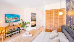 Un dormitorio con cama, televisor, aparador de madera, planta y armario.