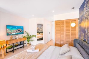 Ein Schlafzimmer mit einem Bett, einem Fernseher, einem Holzschrank, einer Pflanze und einem Kleiderschrank.