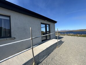 A building with a concrete exterior, a window with a curtain, and a metal railing. - Calla Retreat with stunning views (Roundstone)