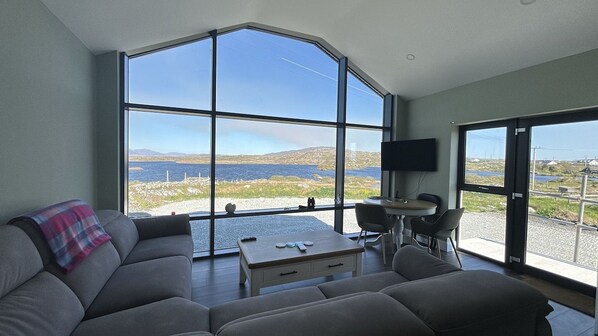A modern living room with a large window, a sofa, a coffee table, and a flat-screen TV.