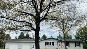 Una casa a un piano con garage, un portico e un albero sullo sfondo.