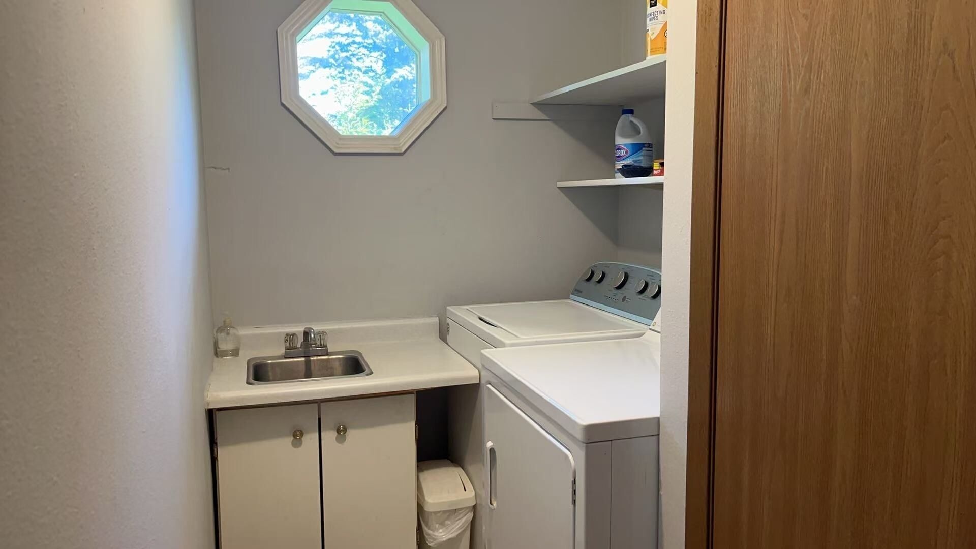 A compact laundry room with a washing machine, a sink, and a window.