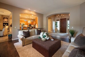 A spacious living room with a sofa, ottoman, and a kitchen in the background. - Luxury Power Ranch Estate- Pool, Spa & Golf Green (Gilbert)