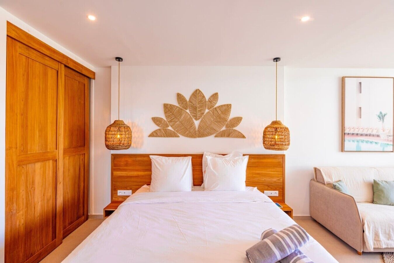 Une chambre à coucher avec un grand lit, une tête de lit en bois, deux lampes fixées au mur, une œuvre d’art murale et un tableau encadré.