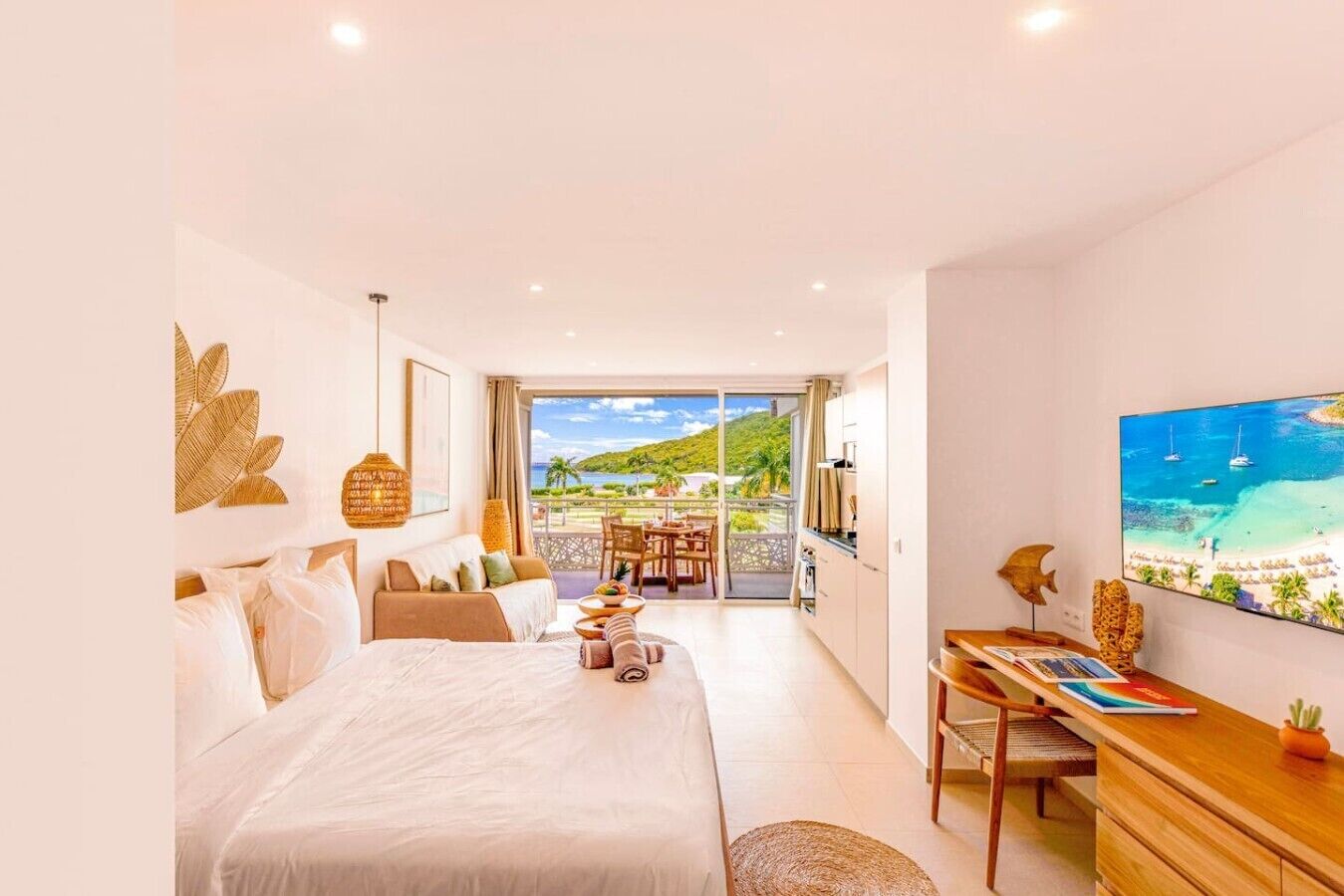 A bedroom with a bed, a desk, a chair, and a view of a beach.