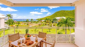 Ein Balkon mit Frühstückstisch, mit Blick auf einen angelegten Garten und das Meer.