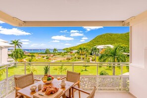 A balcony with a table set for breakfast, overlooking a landscaped garden and a view of the sea. - DDL 624, sea view, beach front, serenity and comfort (Anse Marcel)