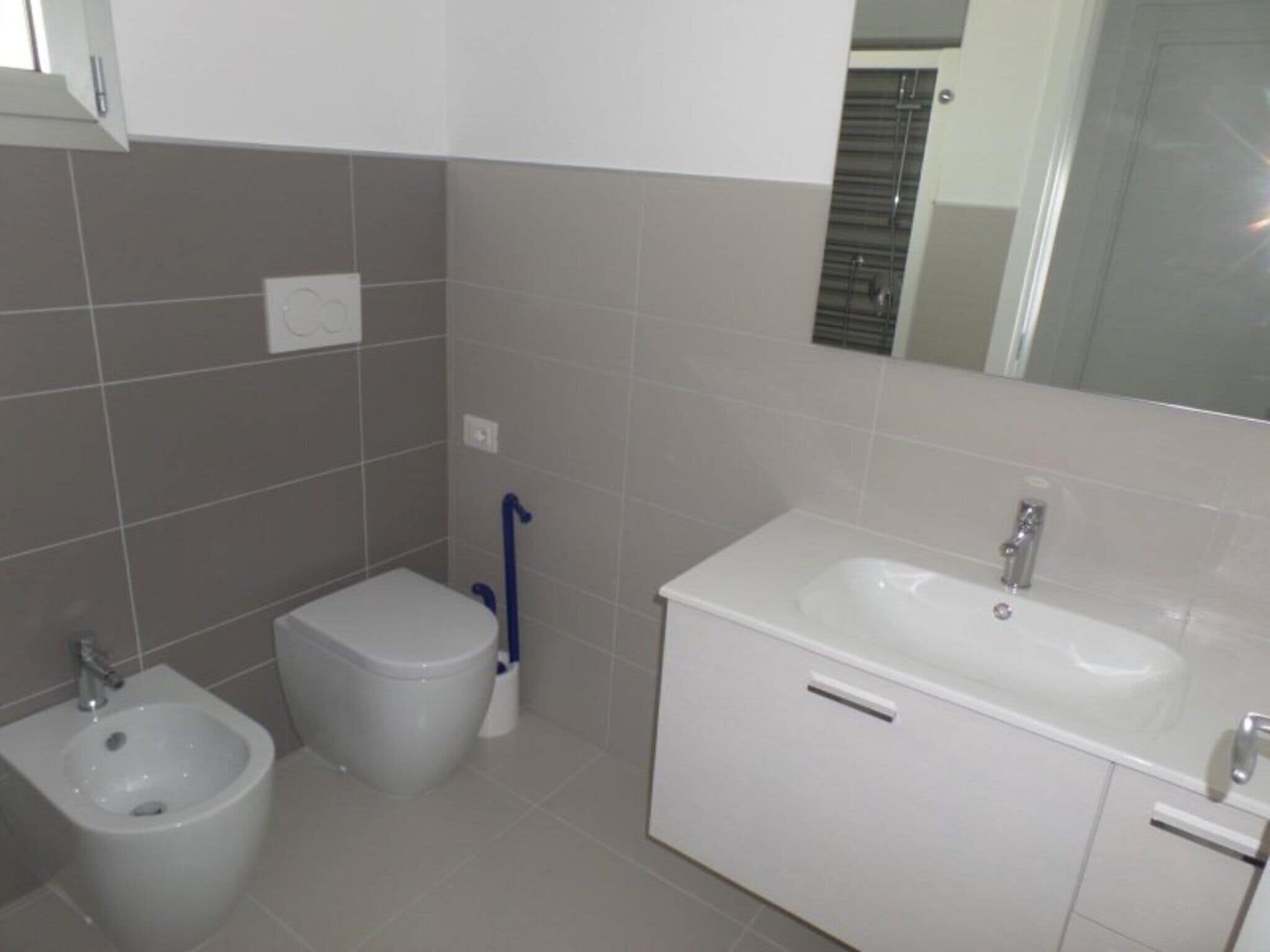 A bathroom with a bidet, toilet, sink, and mirror.