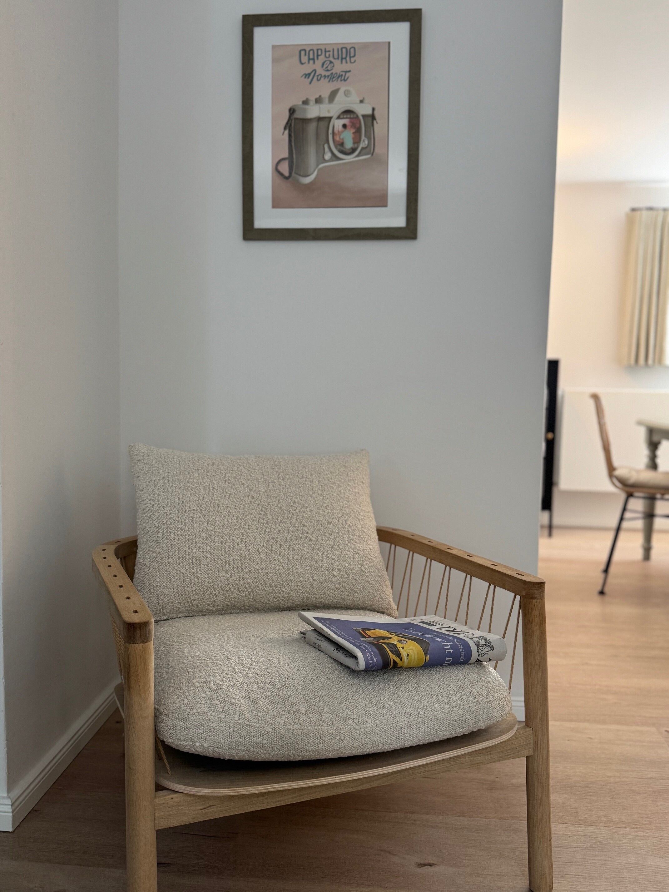 Una silla de madera con un cojín texturizado, un cuadro en la pared y una revista sobre el cojín.