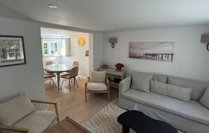 Ein Wohnzimmer mit einer Couch, einem Esstisch mit Stühlen und einem durch einen offenen Durchgang sichtbaren Küchenbereich.