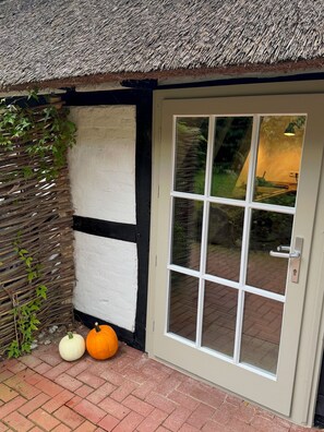 Ein Haus mit Strohdach, einer weiß-schwarzen Fachwerkwand, einer Glastür mit Griff und zwei Kürbissen auf dem Boden.