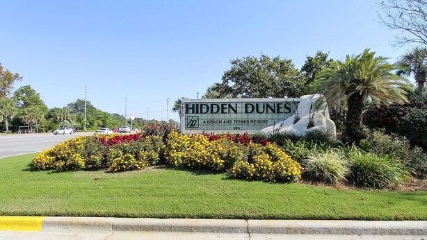 Een bord voor Hidden Dunes Beach and Tennis Resort met een aangelegde tuin ervoor.