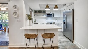 Een moderne keuken met witte kasten, een centraal eiland met twee barkrukken, een roestvrijstalen koelkast en hanglampen.
