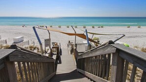 Een houten looppad dat naar een strand leidt, met parasols en ligstoelen.