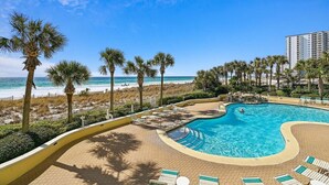 A pool area with lounge chairs, a curved pool, and a beach view. - Jade East 130- Jade Gem (Destin)