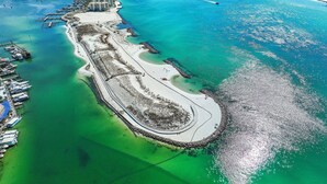 An aerial view of a coastal area with a marina, sandy beach, and clear turquoise waters. - Jade East 130- Jade Gem (Destin)