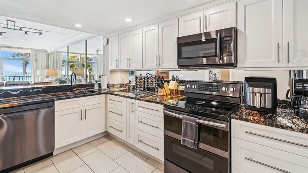 A modern kitchen with white cabinets, stainless steel appliances, and a marble countertop. - Jade East 130- Jade Gem (Destin)