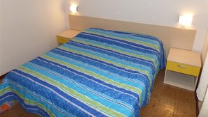 A single bed with a striped bedspread, two bedside tables, and wall-mounted lamps. - Functional Flat in a Quiet Villa in Bibione (San Michele al Tagliamento)