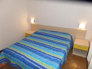 A single bed with a striped bedspread, two bedside tables, and wall-mounted lamps. - Functional Flat in a Quiet Villa in Bibione (San Michele al Tagliamento)