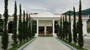 A building with a symmetrical facade, a central entrance with a fountain, and tall trees lining the pathway. - catleya royal club (Pereira)