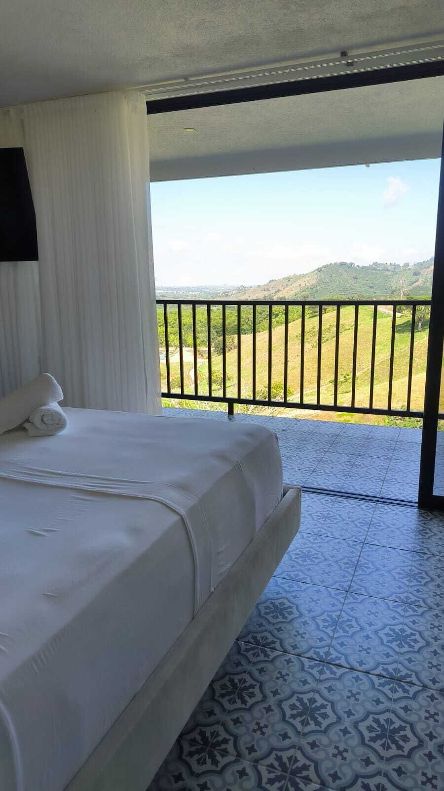 Una camera d'hotel con un letto, vista su un paesaggio verde attraverso un balcone e piastrelle decorative al pavimento.