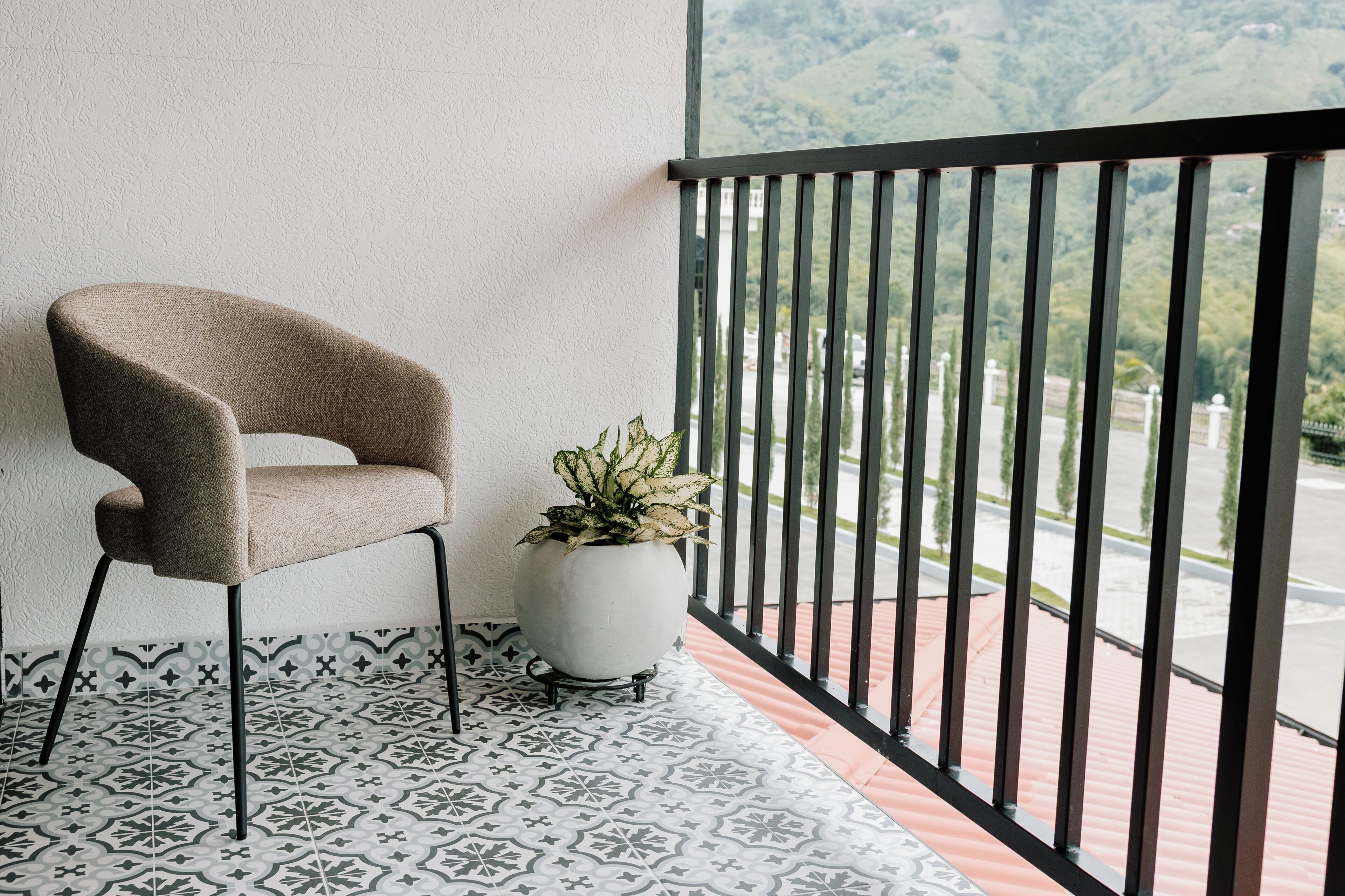 Un balcone con pavimento decorato, una sedia, una pianta in vaso e vista su un paesaggio verde.