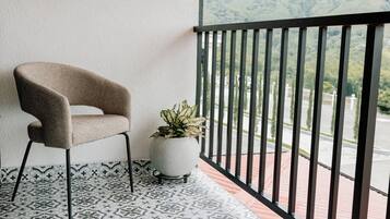 Un balcone con pavimento decorato, una sedia, una pianta in vaso e vista su un paesaggio verde.