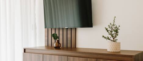 A flat-screen TV mounted on a wooden wall with a plant in a vase on a wooden counter below.