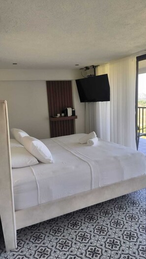 Una habitación de hotel con cama, televisión montada en la pared y ventana con cortinas.