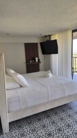 Una habitación de hotel con cama, televisión montada en la pared y ventana con cortinas.