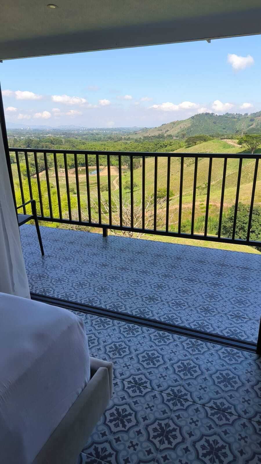 Un balcone con pavimento decorato e ringhiera in metallo, affaccia su un paesaggio verdeggiante con colline.