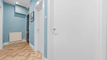 A hallway with a white door, a radiator, and a herringbone-patterned floor.