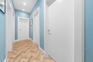 Un couloir avec un plancher en bois, des portes blanches et des murs bleus.