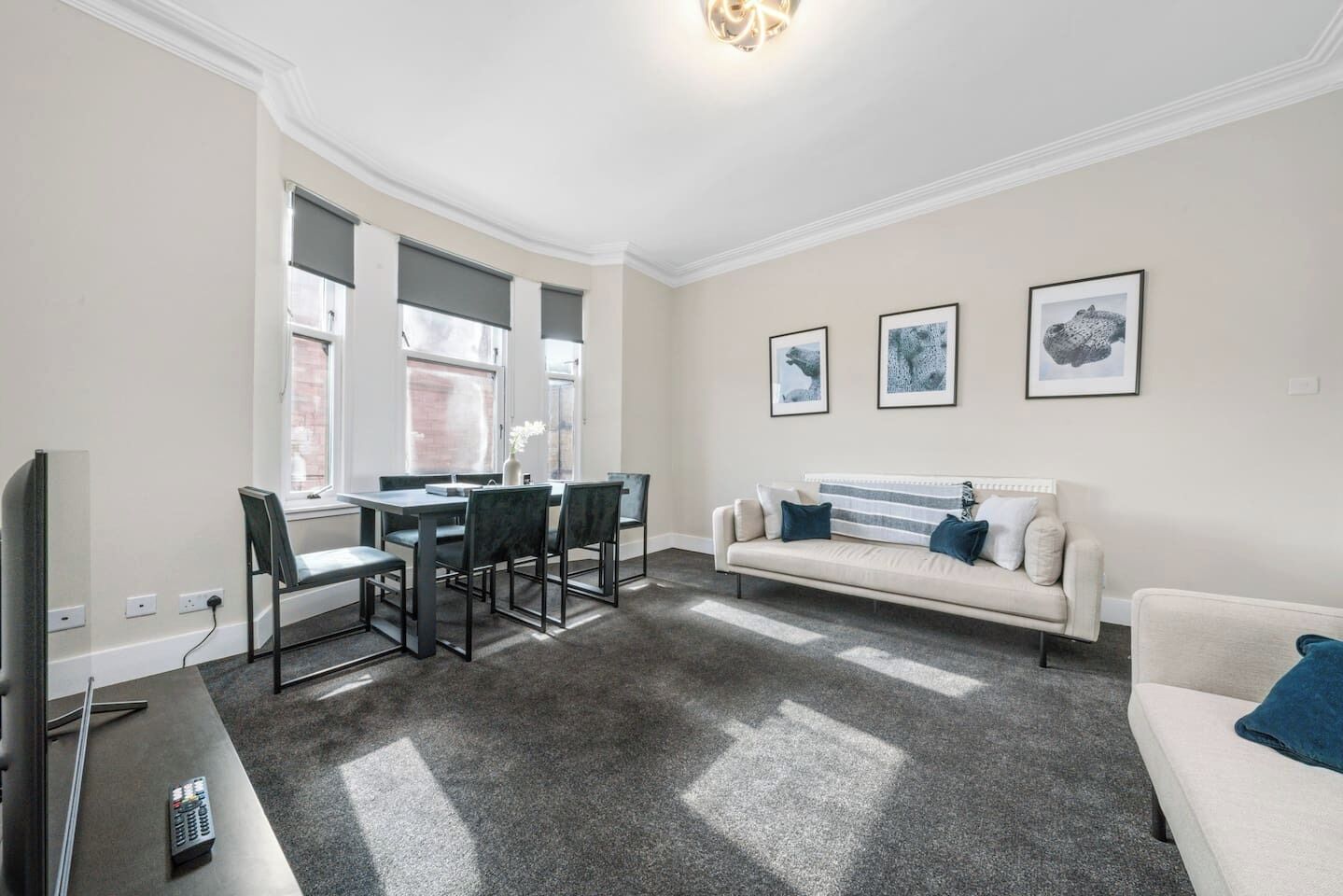 A living room with a sofa, a dining table with chairs, a TV, and artwork on the wall.
