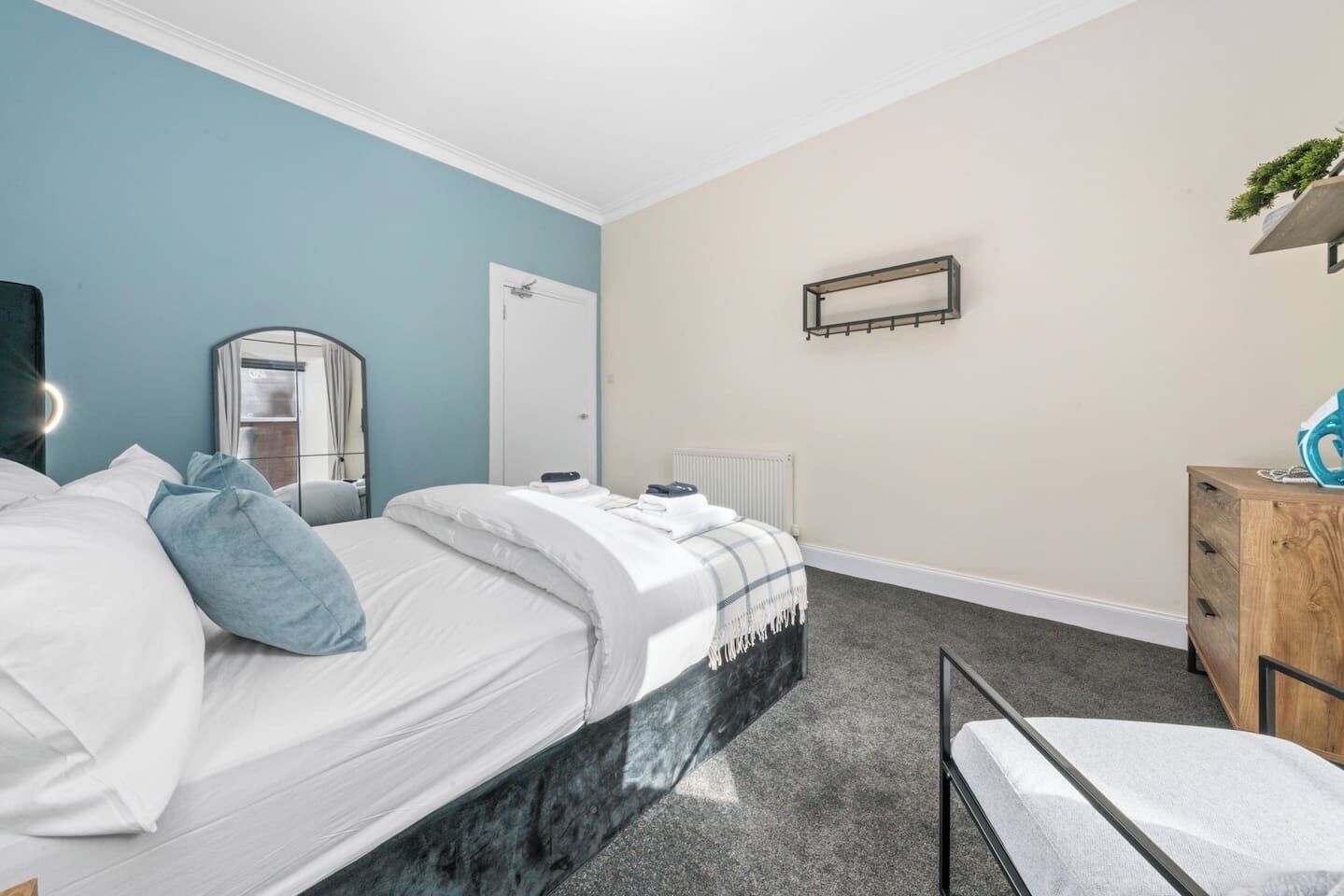 A hotel room with a bed, a bedside table, a mirror, a radiator, and a dresser.