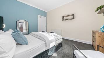 A hotel room with a bed, a bedside table, a mirror, a radiator, and a dresser.
