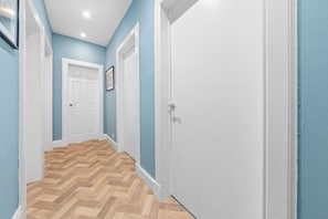 A hallway with wooden flooring, white doors, and blue walls.