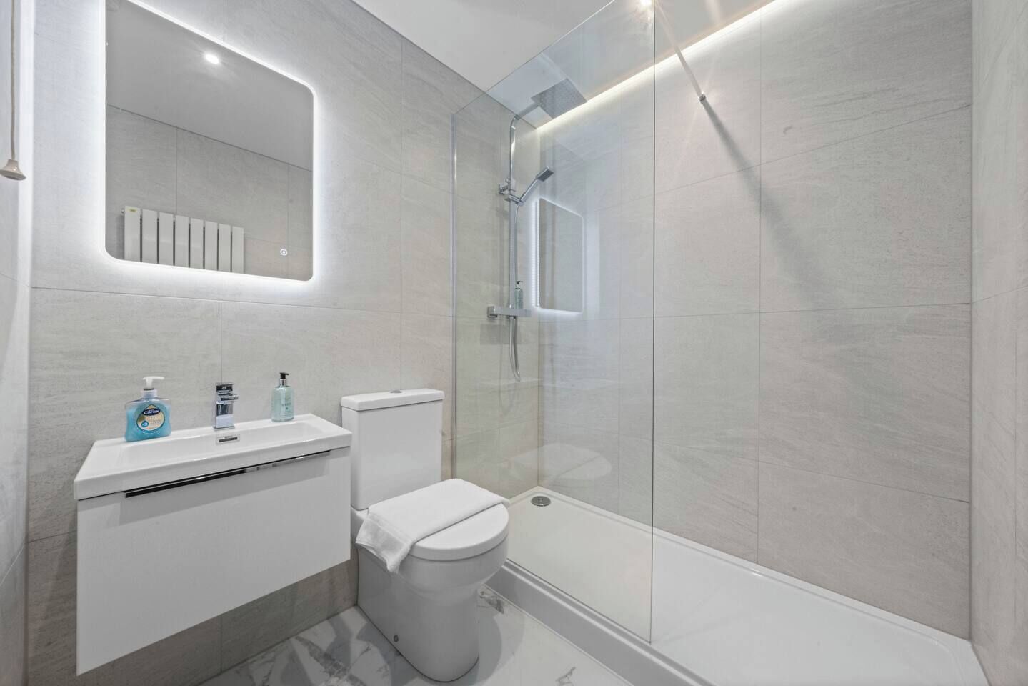 Une salle de bain moderne avec une douche à parois de verre, un lavabo blanc avec un miroir au-dessus et des toilettes.