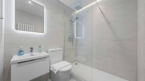 Ein modernes Badezimmer mit einer begehbaren Glasdusche, einem weißen Waschbecken mit Spiegel darüber und einer Toilette.