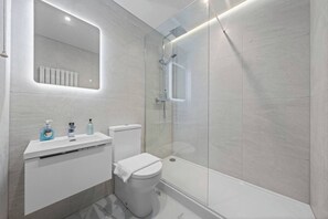 A modern bathroom with a glass-enclosed shower, a white sink with a mirror above it, and a toilet. - Falkirk Urban Apartment - Free Parking (Falkirk)