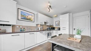 A modern kitchen with white cabinets, a wooden countertop, a dining table, and a hanging light fixture. - Modern Stirling Apartment - Free Parking (Stirling)