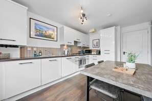A modern kitchen with white cabinets, a wooden countertop, a dining table, and a hanging light fixture. - Modern Stirling Apartment - Free Parking (Stirling)
