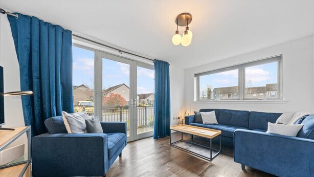 A modern living room with a blue sofa set, a coffee table, and a large sliding glass door leading to an outdoor area. - Modern Stirling Apartment - Free Parking (Stirling)