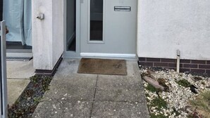 A building entrance with a grey door, a small step leading up, a doormat, and a sign indicating integrated systems. - Modern Stirling Apartment - Free Parking (Stirling)