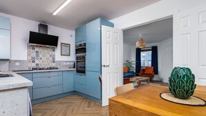A modern kitchen with blue cabinets, a herringbone floor, and a dining area with a wooden table and chairs. - Modern 2-Bed Stirling House | Driveway Parking (Stirling)