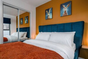 Une chambre d’hôtel avec un grand lit, une tête de lit bleue, du linge de lit blanc et deux tableaux accrochés au mur.