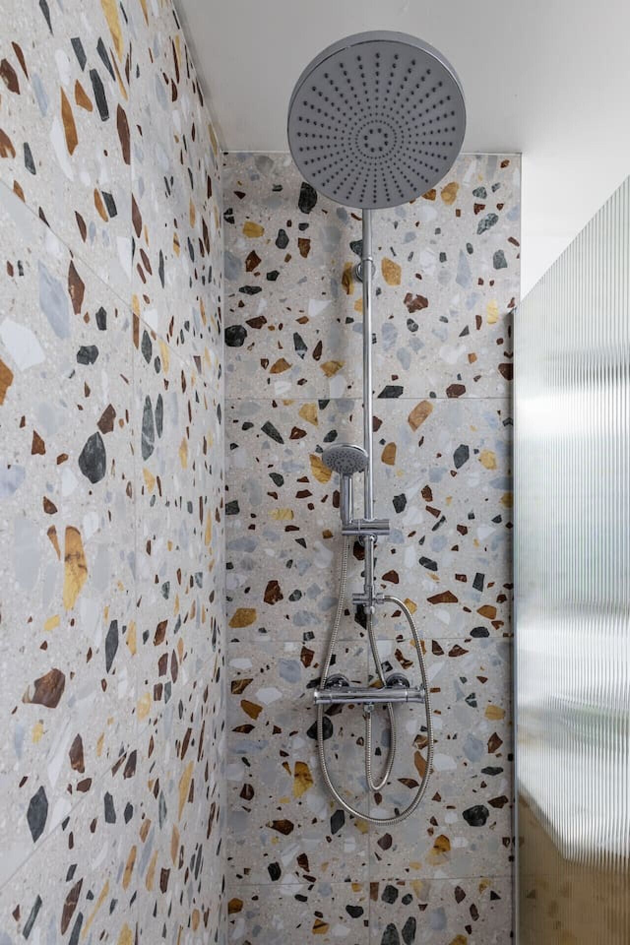 A shower with a circular head and a handheld showerhead, set against a speckled wall.