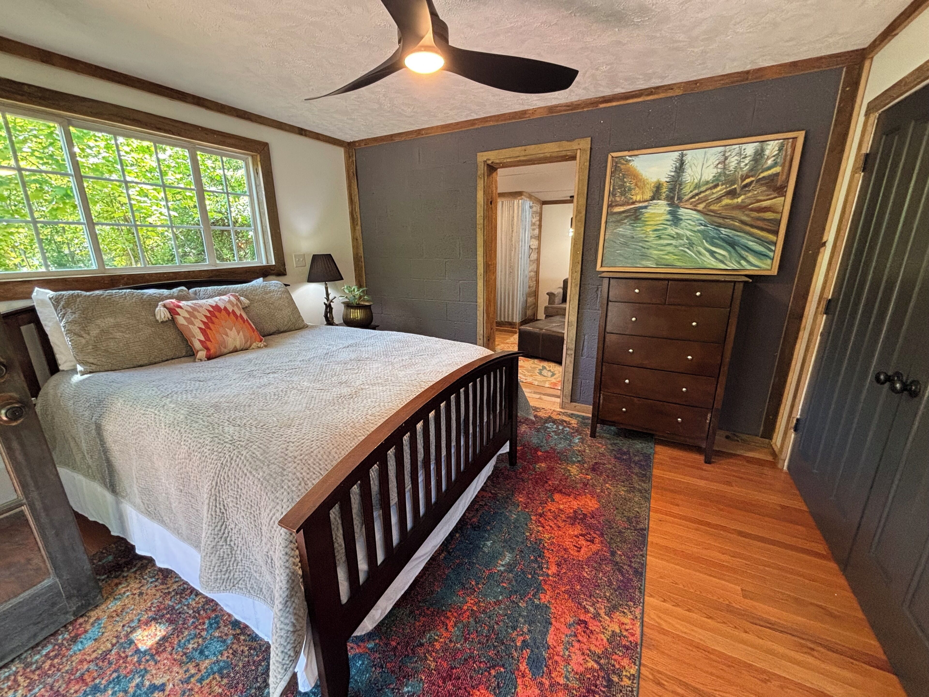 Une chambre à coucher avec un lit, un ventilateur de plafond, une commode, un tableau et une fenêtre.