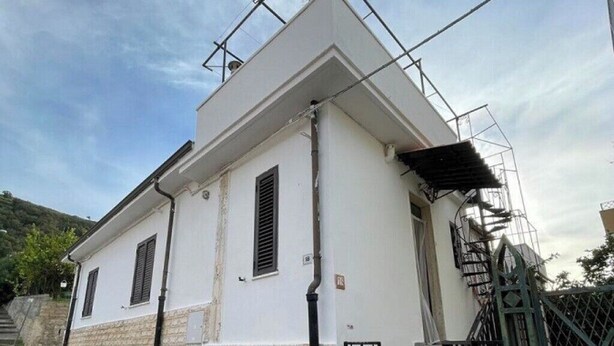 A two-story building with a white facade, a brick base, and a metal staircase leading to the entrance. - Casa Fedafa  (Parghelia)
