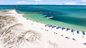 Een strand met wit zand, helder turquoise water en enkele boten.